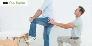 A man with piriformis syndrome is standing and hugging his left knee as the doctor examines him behind him