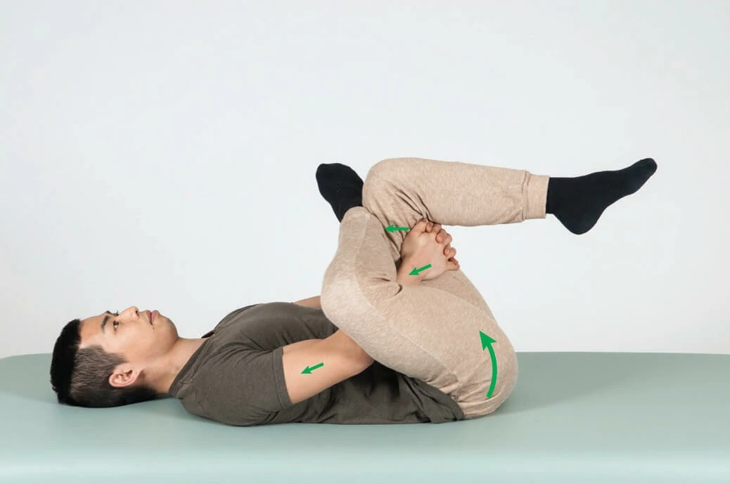 A male is lying on a treatment bed, undergoing stretching exercises to heal piriformis syndrome