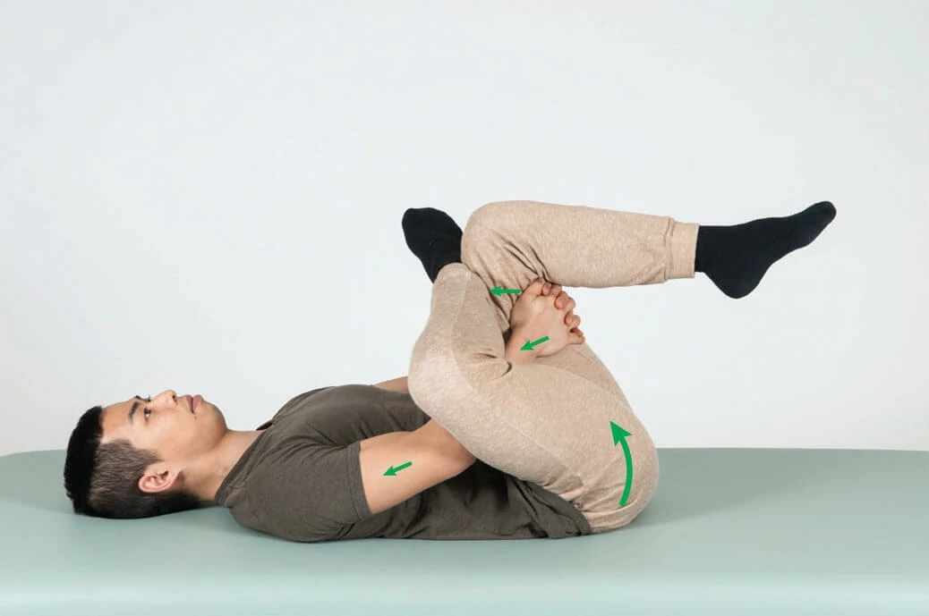 A male undergoes supine stretching therapy on a treatment bed to alleviate piriformis syndrome