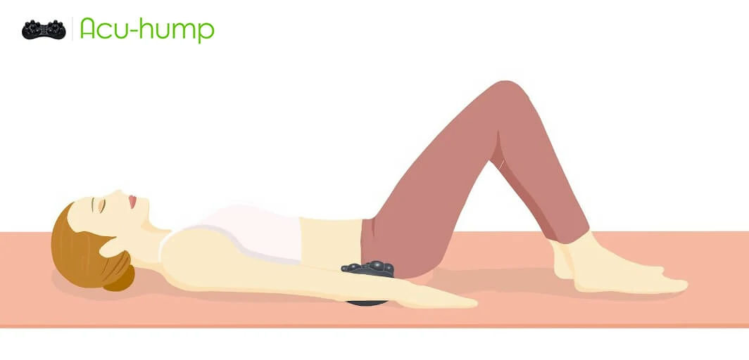 A woman lying on her back on a yoga mat with an Acu-hump tool on her sacurm, which massages and stretches her SI Joint to heal SI pain sciatica hip pain