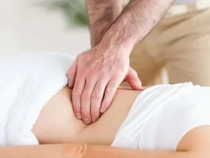 The masseur presses the patient's right QL muscle with both hands