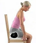 A woman places an Acu-hump on an office chair and sits on it to massage her tight buttocks after long periods of sitting