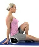 A woman places the Acu-hump on the floor and sits on it to perform glute muscle massages and hamstrings stretches