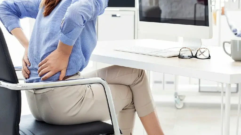 A woman‘s hands on her back, was experiencing sciatica, an attack of lower back pain, from sitting for long periods of time